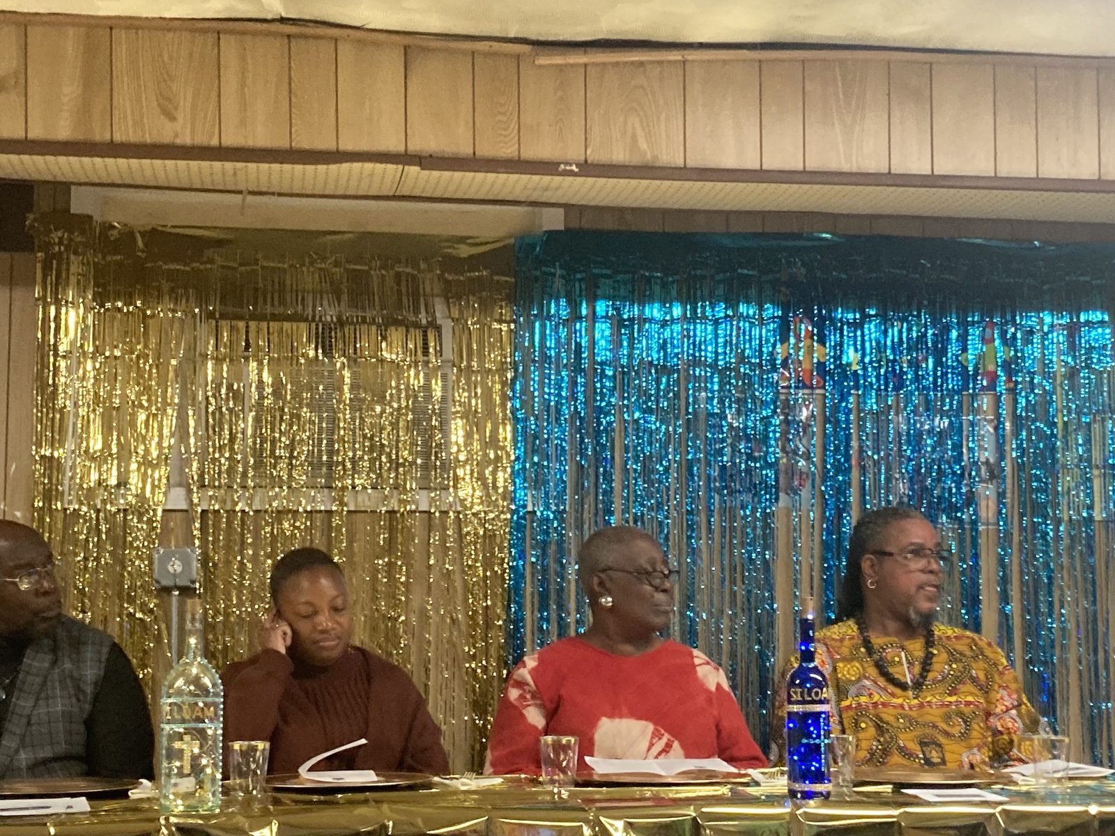 Four people seated at a head table in front of a gold and teal backdrop