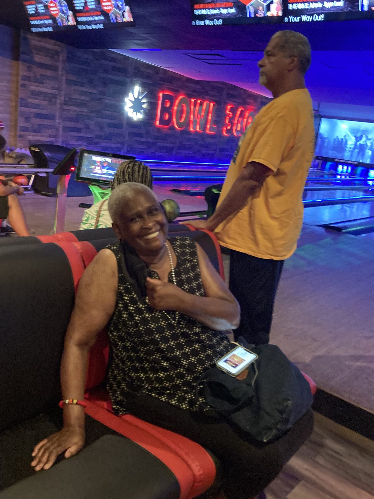 A woman smiling from a bench at a bowling alley