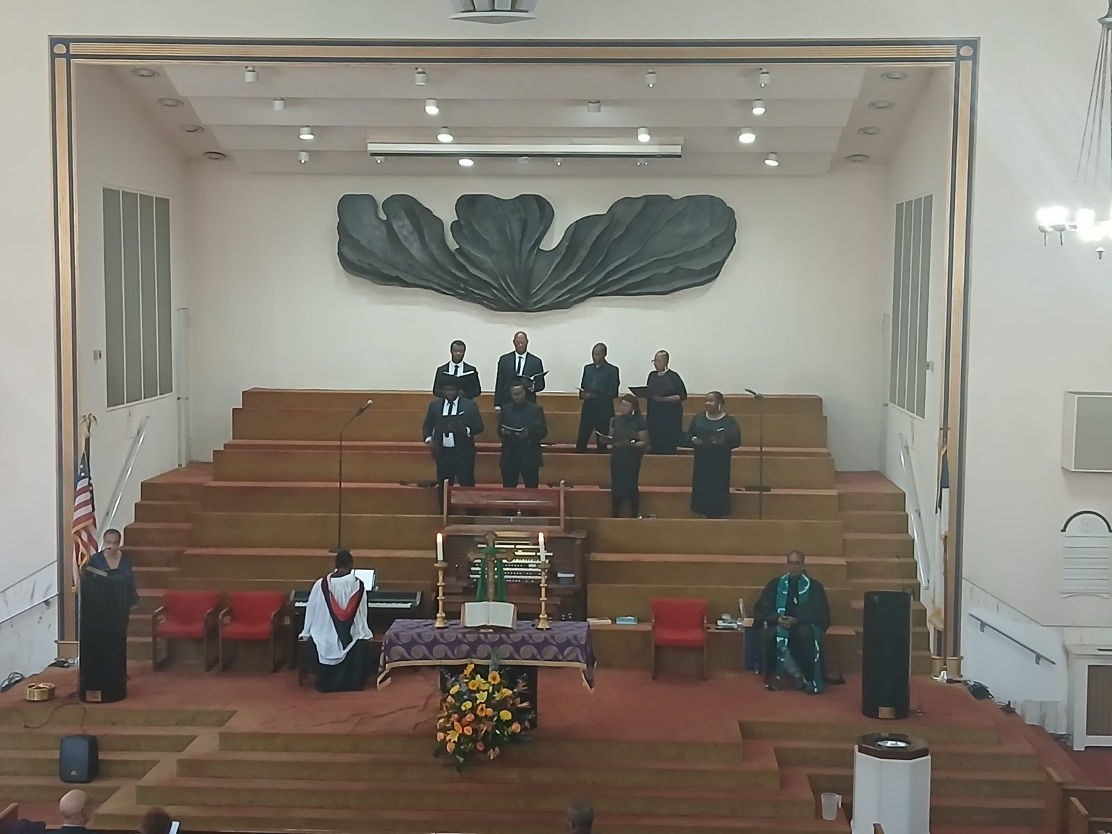 The choir standing in the loft during worship, beneath the large carved sculpture on the sanctuary wall
